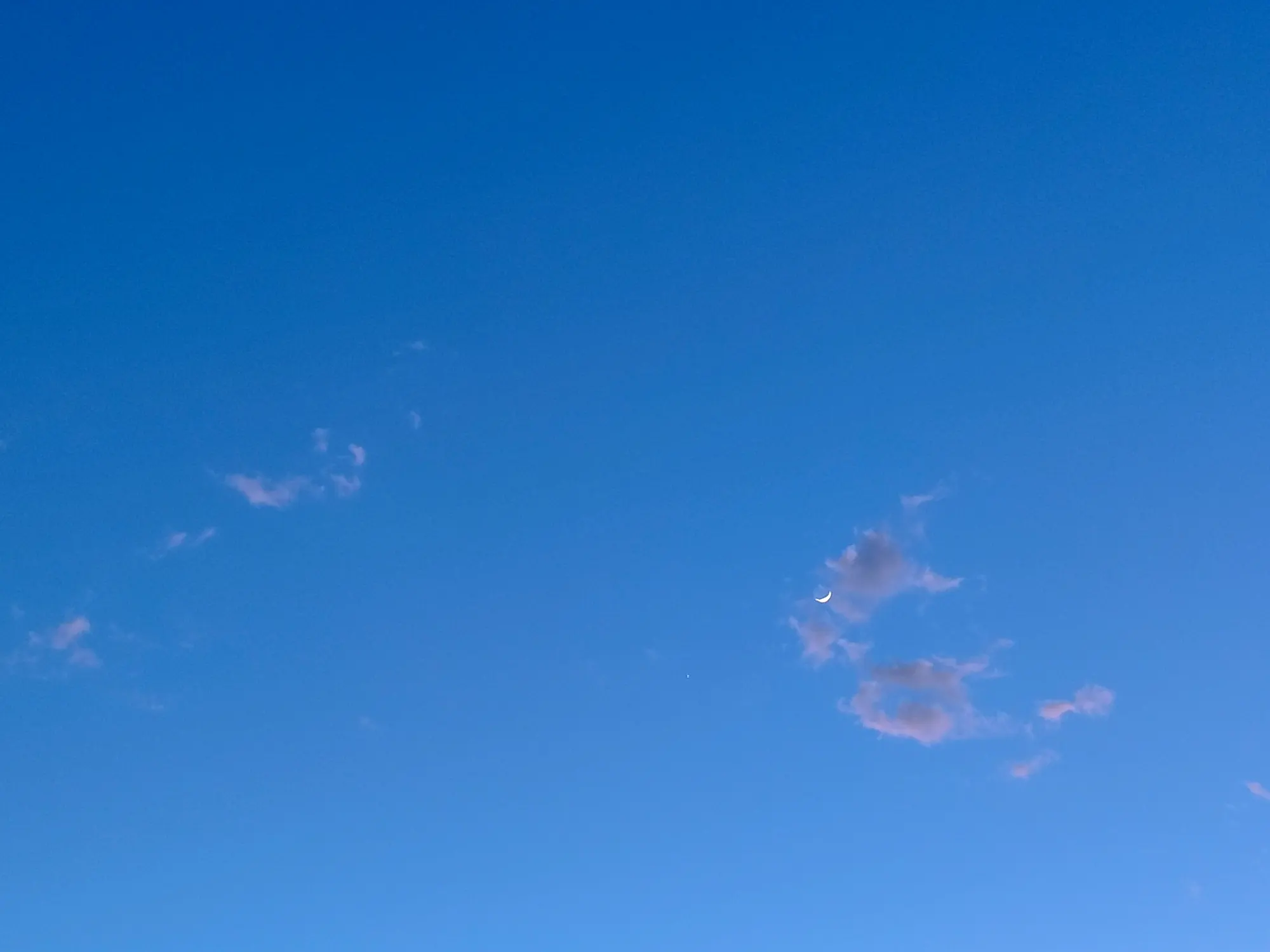 A clear deep blue sky with a slim crescent moon and a few thin clouds catching the last light.
