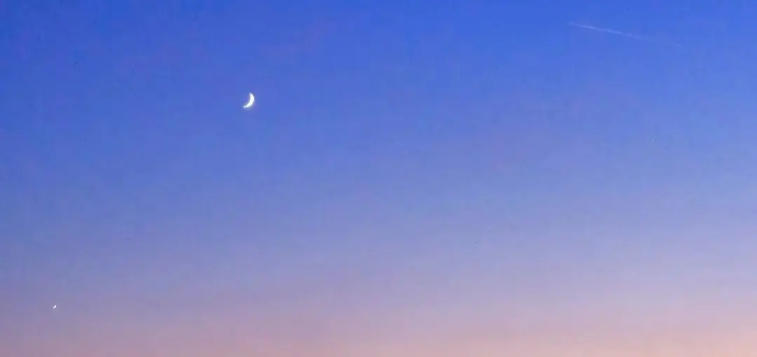 A wide band of dusk sky grading from blue to amber, holding a crescent moon and a single bright planet.