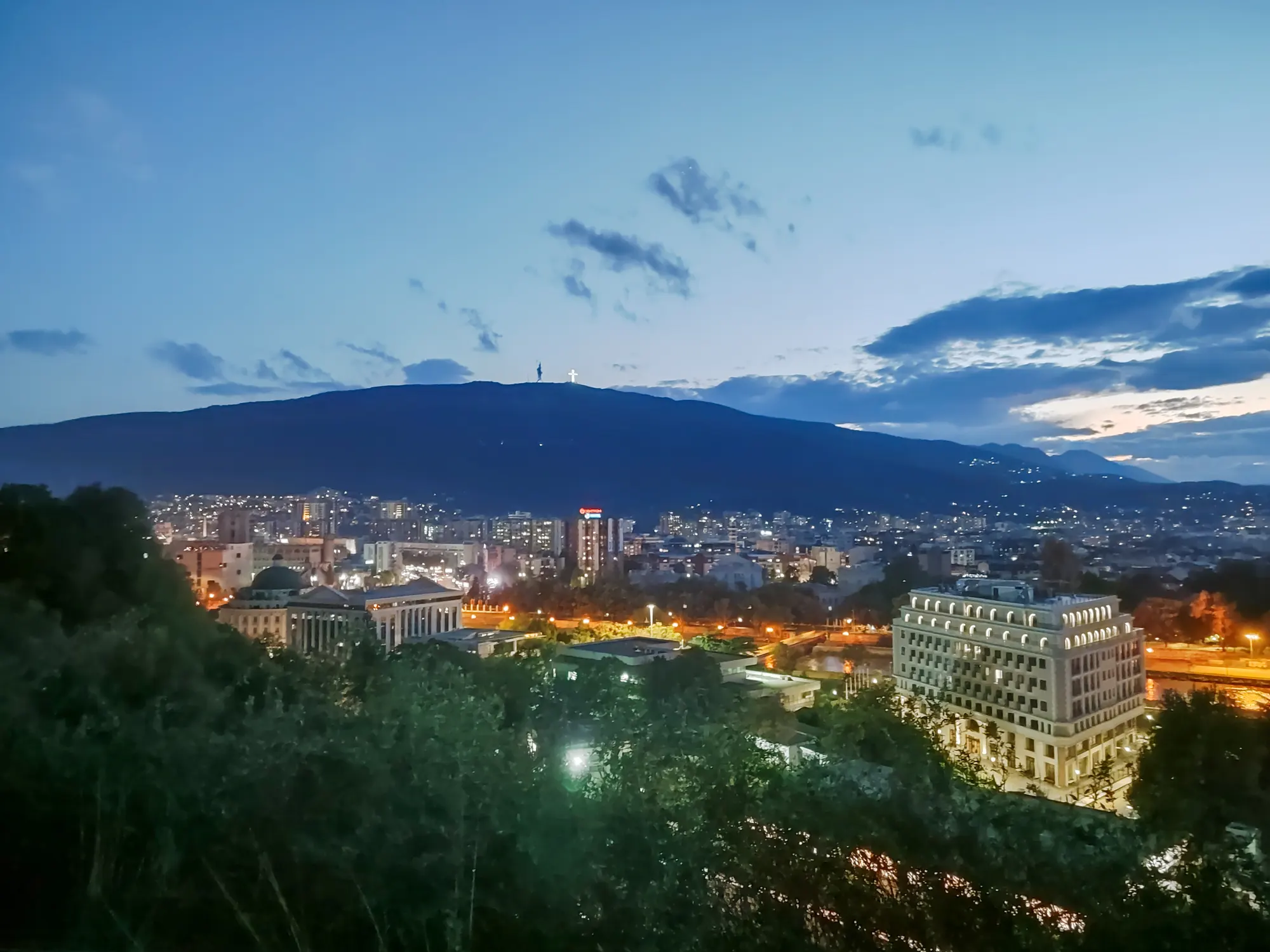 The same view over Skopje earlier in the evening, the sky still blue, the city lights just coming on below Mount Vodno.